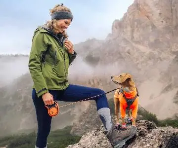 uma senhora nas montanhas com o seu canino e uma trela